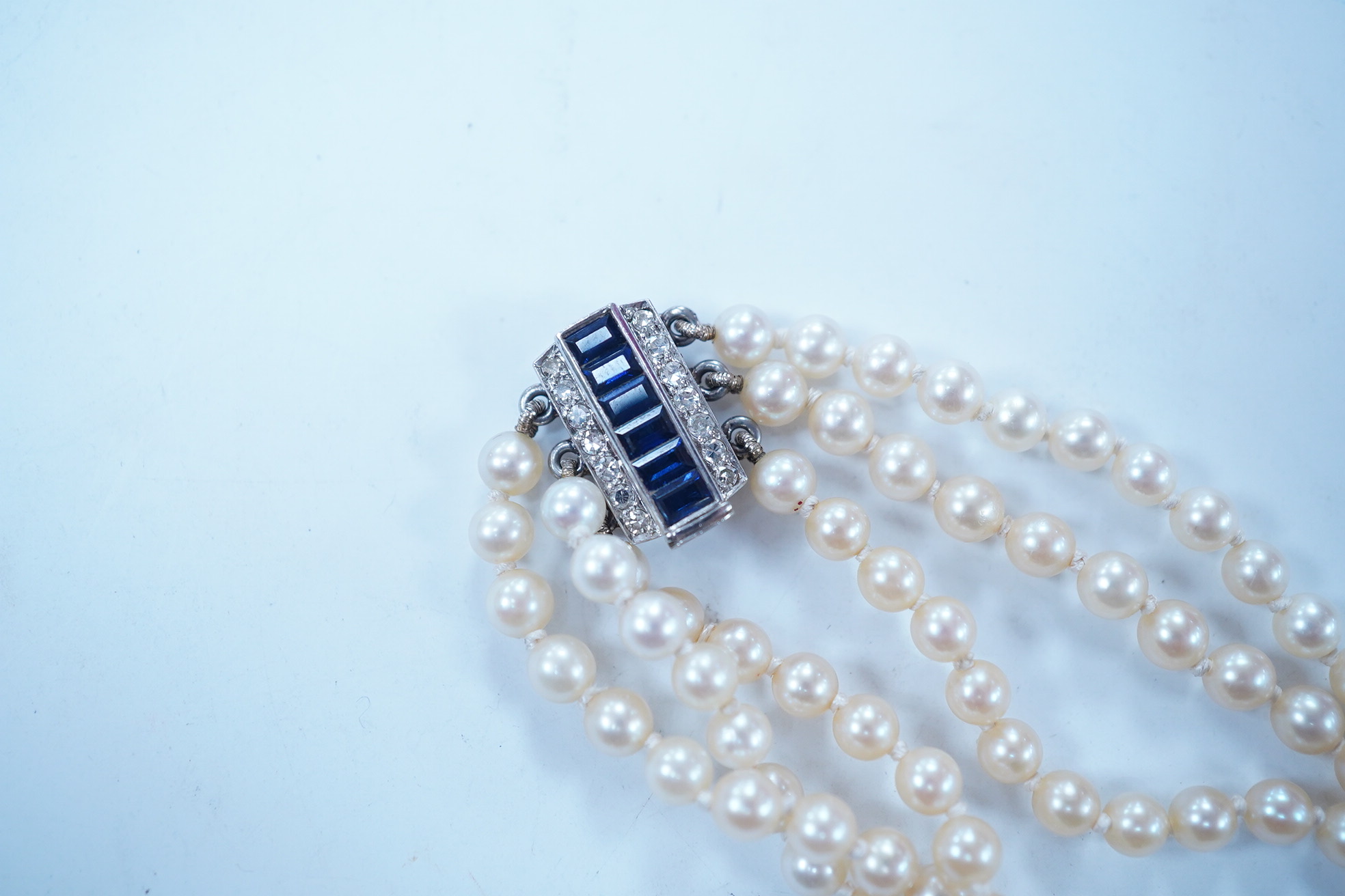 A triple strand cultured pearl choker necklace, with sapphire and diamond cluster set rectangular white metal clasp, 32cm. Condition - fair to good